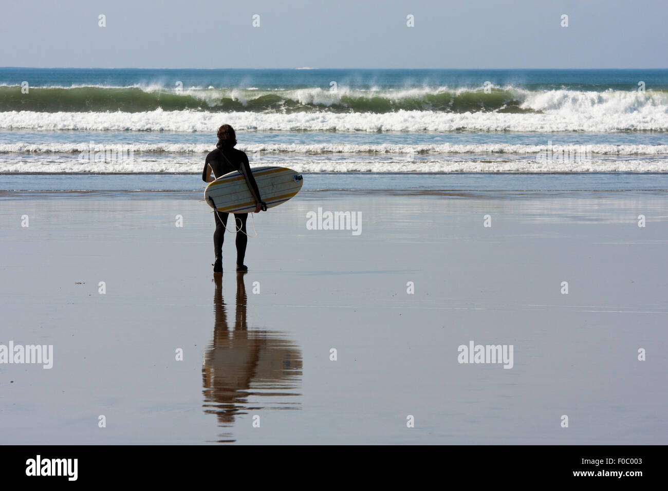 Man with surfboard regardant vagues à la plage de Lahinch, Irlande Banque D'Images