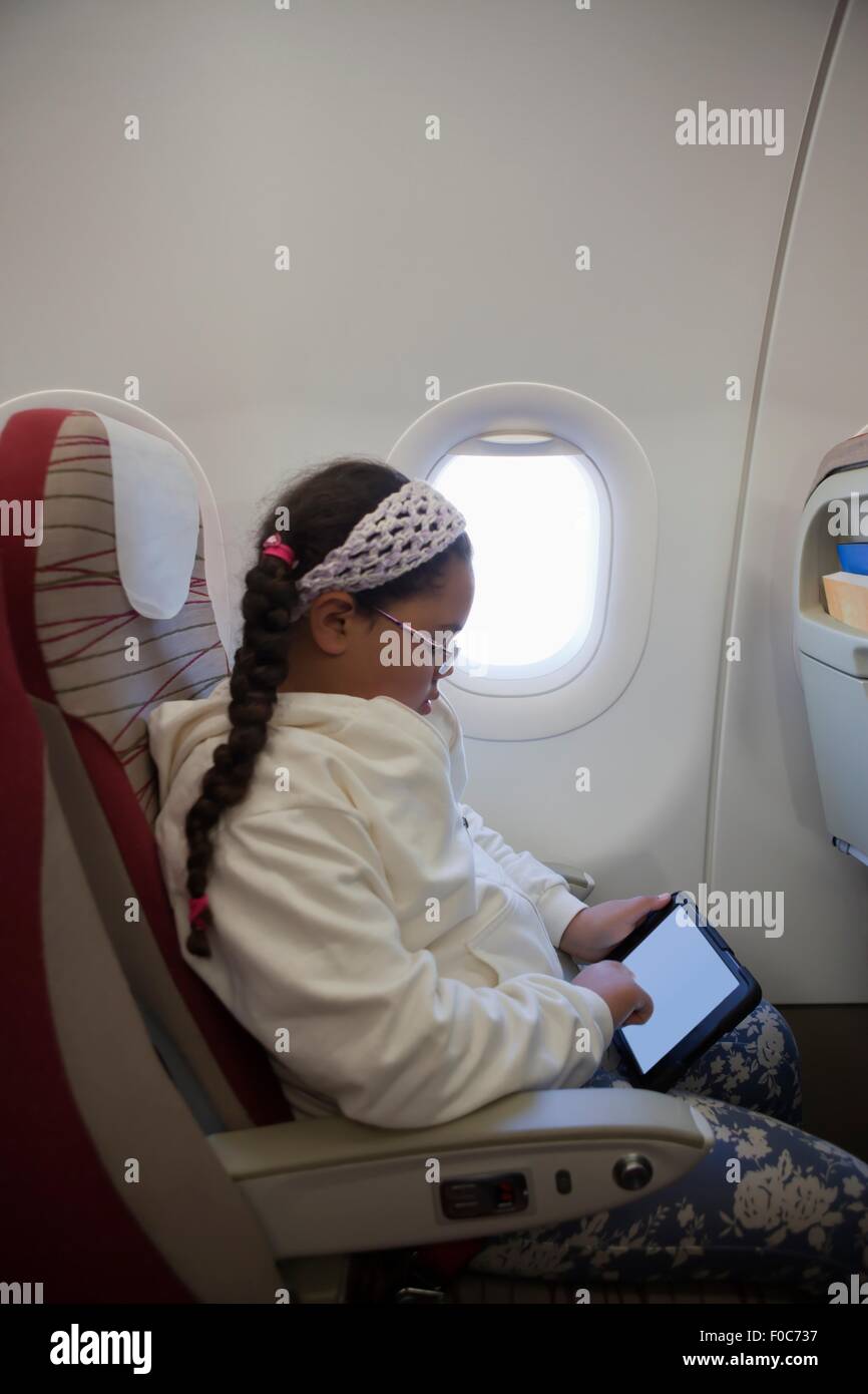 Jeune fille assise sur le siège on airplane using digital tablet Banque D'Images
