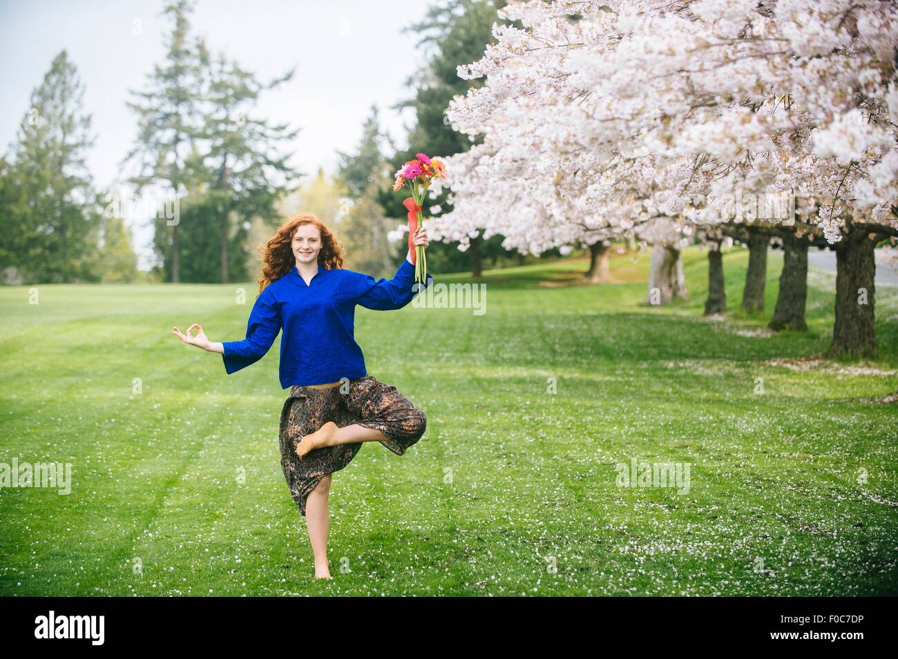 Portrait of young woman practicing yoga tout en maintenant bouquet de fleurs dans le parc Banque D'Images