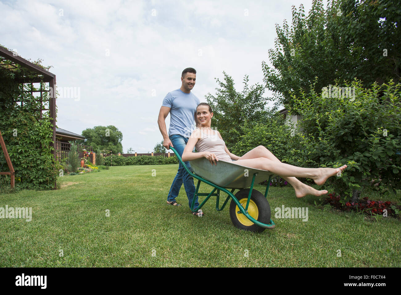 Man pushing wheelbarrow at girlfriend in backyard Banque D'Images