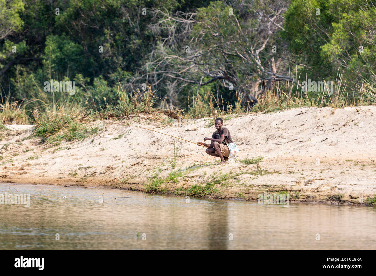 Vie locale : indigènes africains riverside pêcheur sur les rives de la rivière Zambèze, Mosi-Oa-Tunya National Park en Zambie, la pêche au moyen d'un poteau en bois Banque D'Images