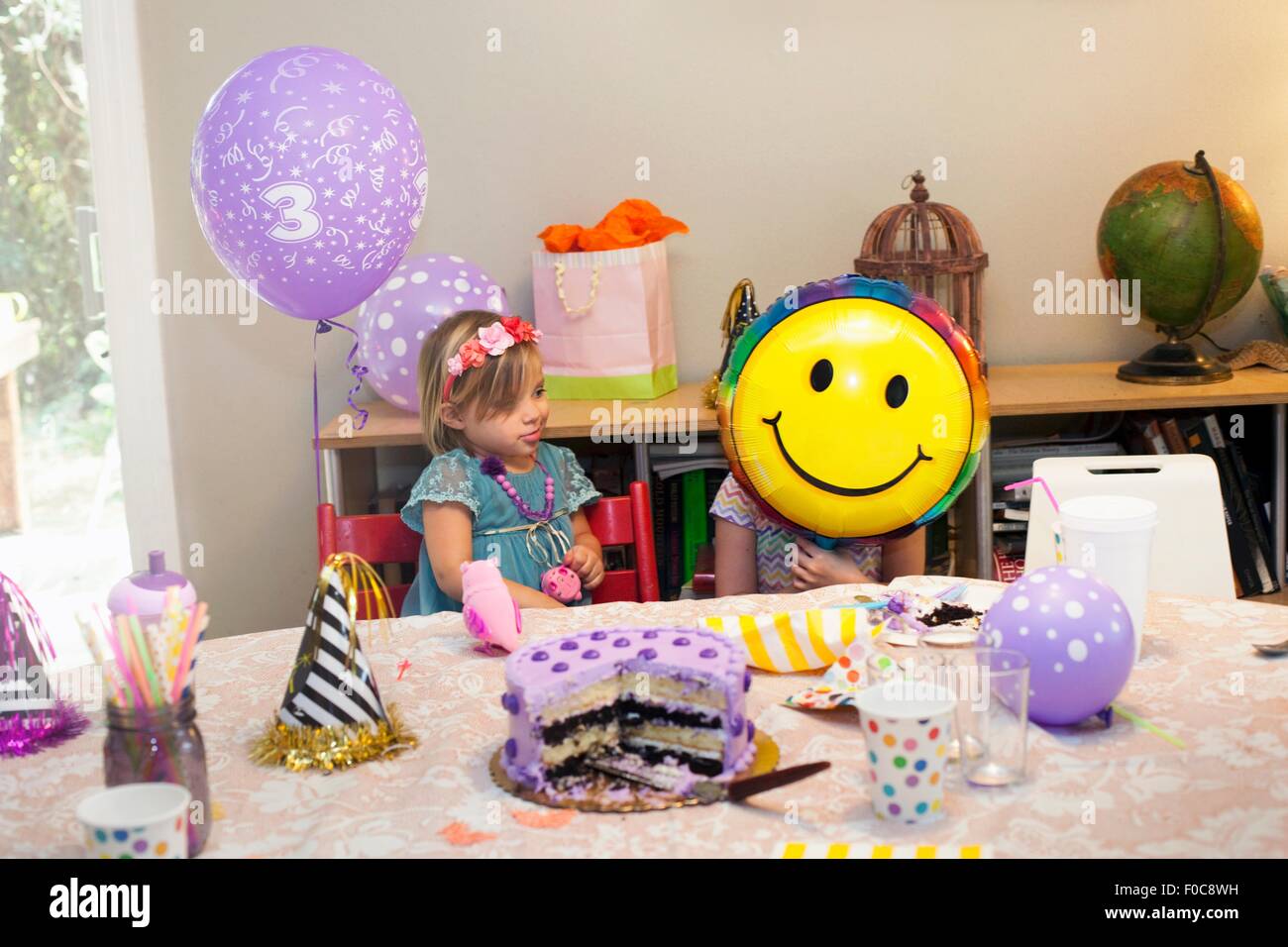 Deux Filles Assis A Table D Anniversaire Avec Gateau Jouant Avec Smiley Face Balloon Photo Stock Alamy