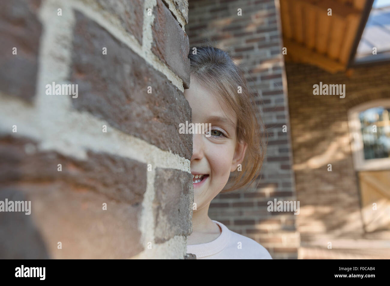 Portrait of smiling girl se cacher derrière un mur de briques Banque D'Images