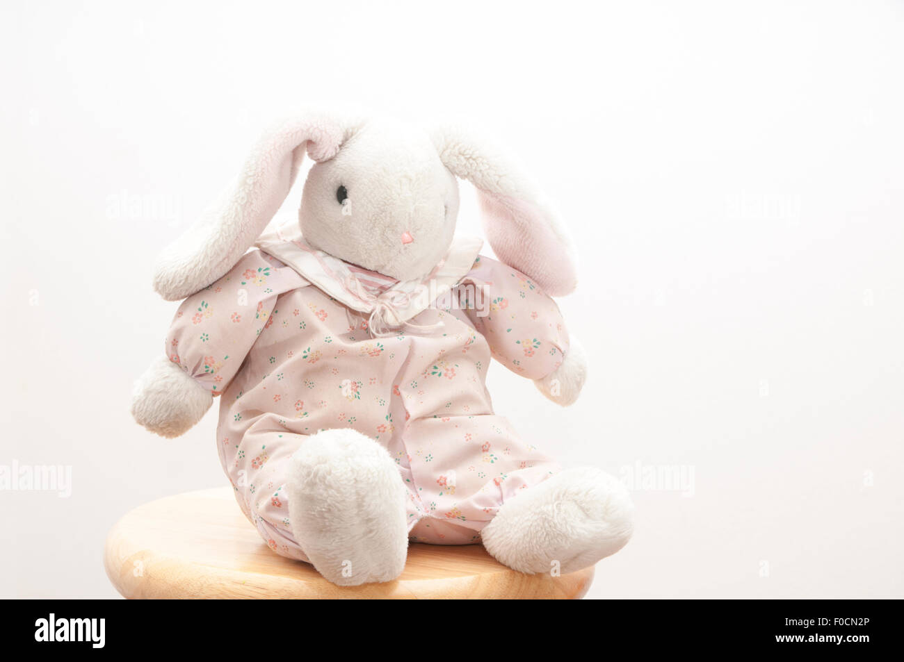 Lapin en peluche rétro assise sur un tabouret avec un fond blanc. Banque D'Images