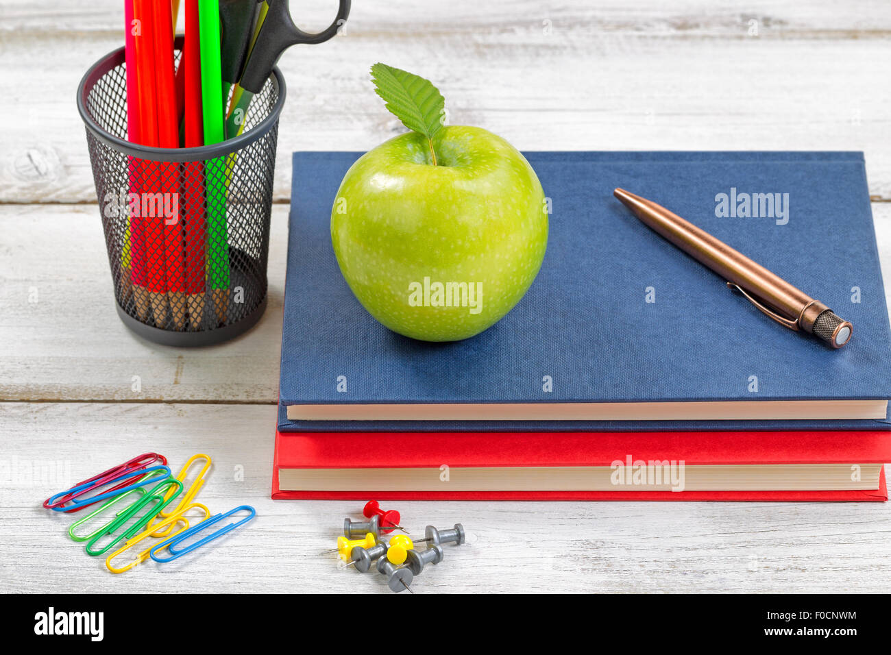 Une pomme verte, books, stylo, trombones, punaises et un contenant d'alimentation sur le dessus de bureau blanc. Concept de l'éducation. Banque D'Images