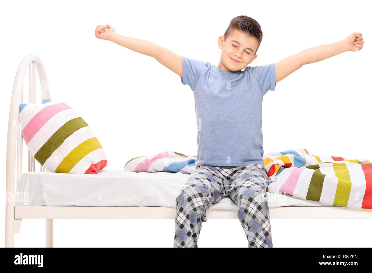 Mignon petit garçon en pyjama qui s'étend lui-même assis sur un lit isolated on white Banque D'Images