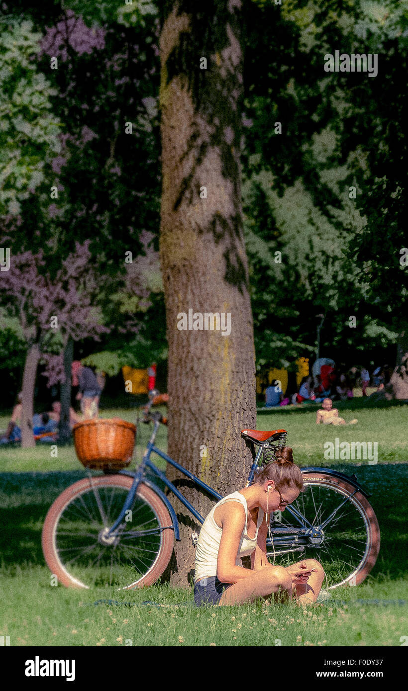 Jeune femme listening to MP3 player assis dans l'herbe dans le parc Montanelli, Milan, Italie. Banque D'Images