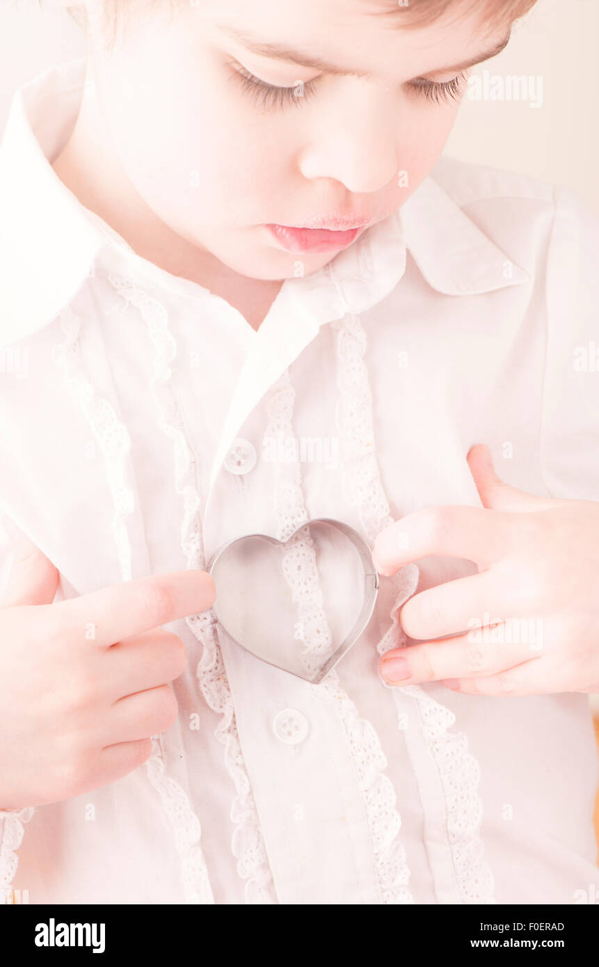 Little girl holding emporte-pièce en forme de cœur dans ses mains. Image conceptuelle de l'enfance, l'amour et l'affection. Banque D'Images