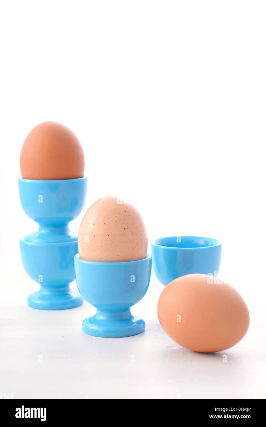 Scène de petit-déjeuner avec des oeufs en bleu egg cups sur table en bois blanc vintage avec l'exemplaire de l'espace pour votre texte ici. Banque D'Images