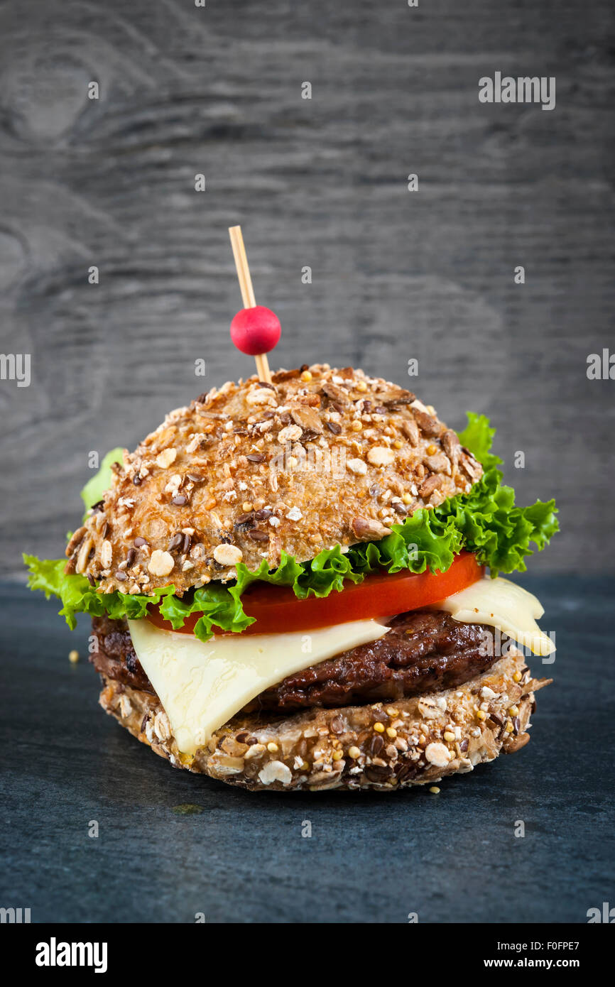 Hamburger gourmet avec fromage suisse et des légumes frais sur pain multigrains sur fond sombre Banque D'Images
