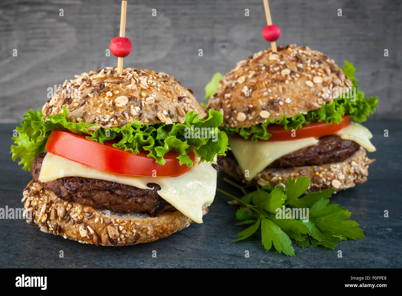 Deux hamburgers gastronomiques avec le fromage suisse et des légumes frais sur les petits pains multigrains sur fond sombre Banque D'Images