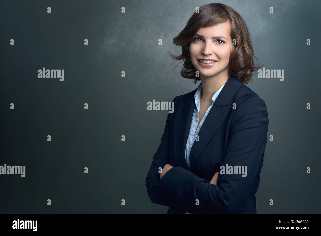 La moitié d'un projectile de corps Happy Young Businesswoman Smiling at the Camera avec sa main sur son menton contre le mur gris. Banque D'Images