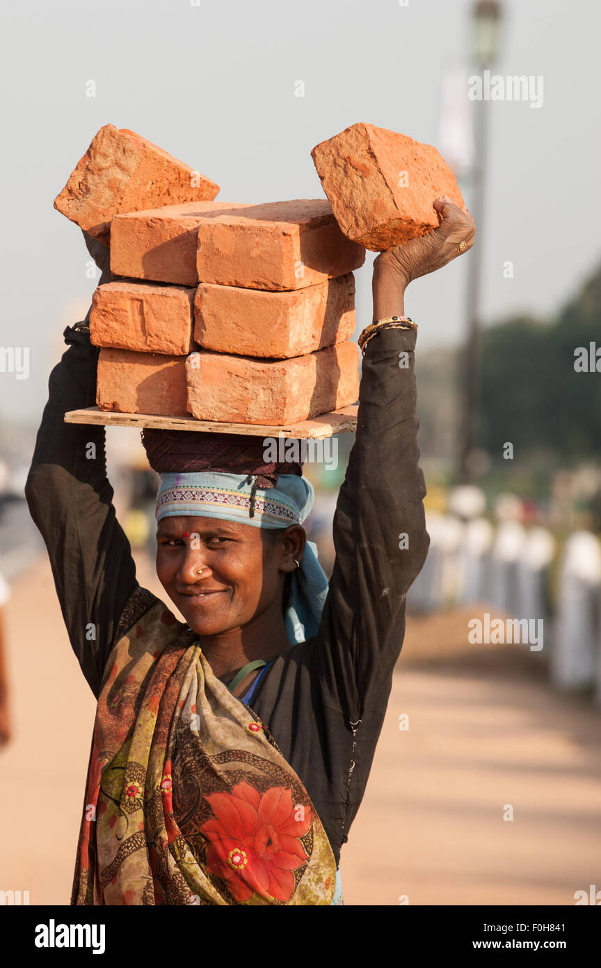 Delhi, Inde. Femme transportant huit briques sur sa tête en souriant. Banque D'Images