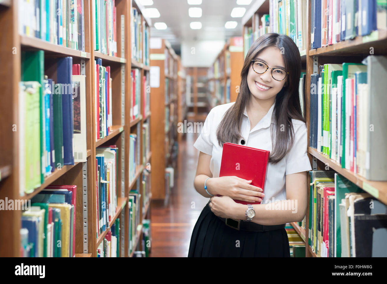 Étudiant asiatique en uniforme la lecture dans la bibliothèque à l'université Banque D'Images