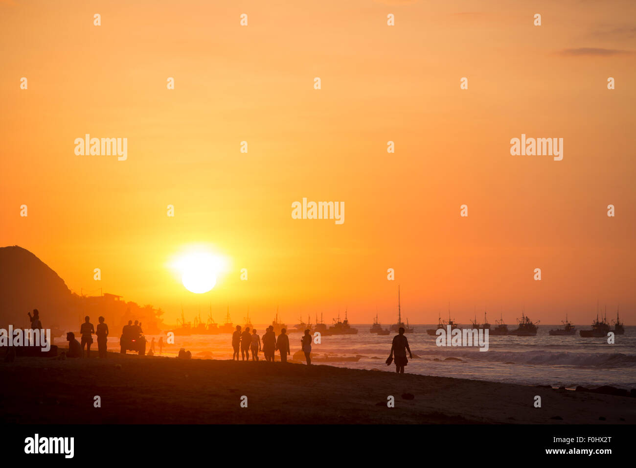 Silhouette de personnes sur la plage de Mancora au cours d'un fantastique coucher du soleil orange avec le port en arrière-plan. Pérou 2015 Banque D'Images