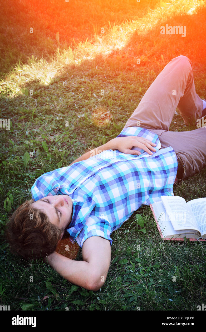Jeune homme se repose sur l'herbe avec un livre Banque D'Images