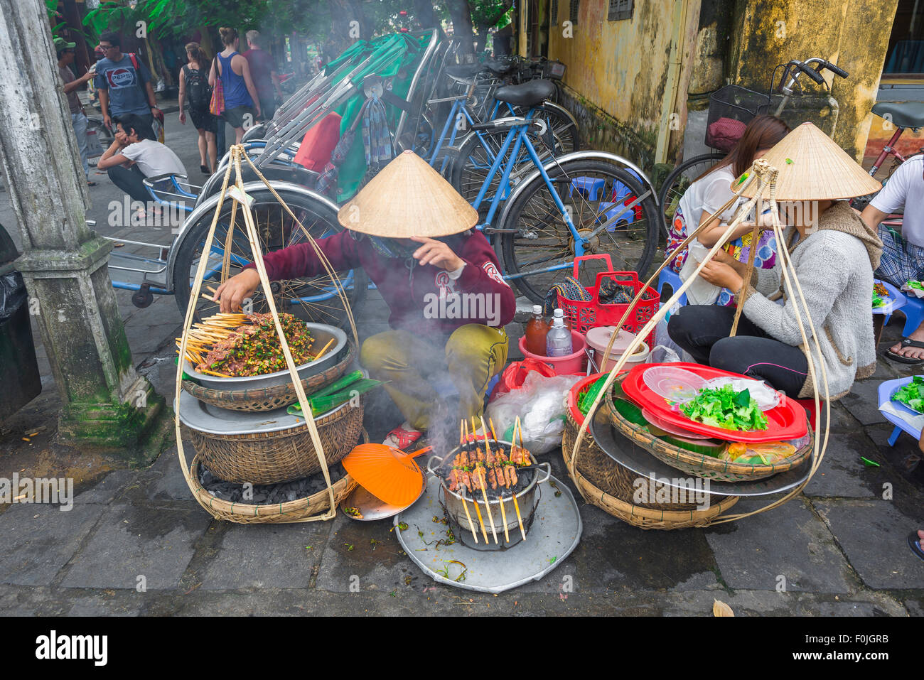 Vietnam Street food, vue de deux femmes grillant des kebabs de porc dans la rue près du front de mer à Hoi an, au centre du Vietnam. Banque D'Images