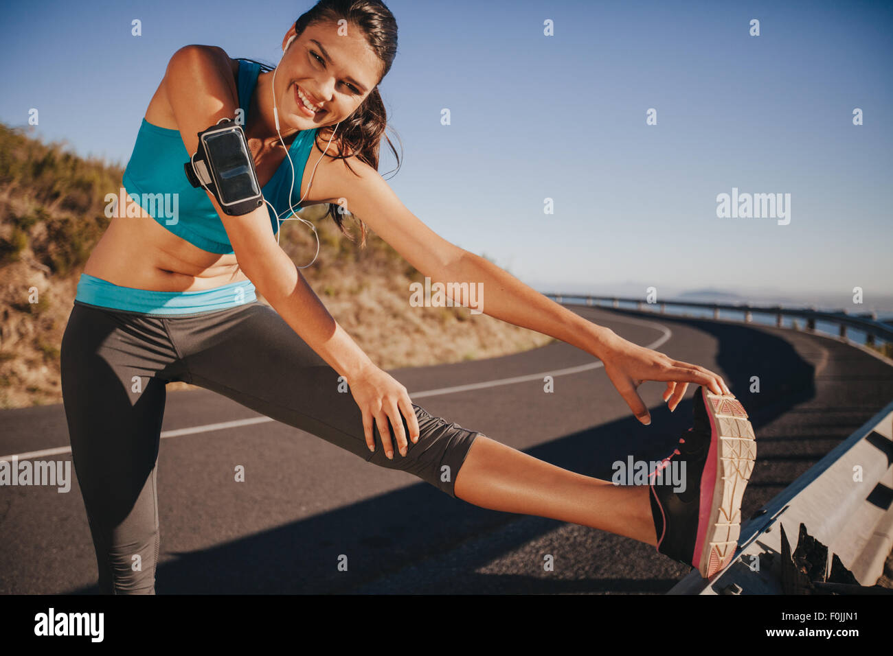 Athlète féminin s'étend ses jambes avant d'exécuter en plein air. Jeune femme fit l'échauffement pour une course sur route de campagne. Banque D'Images