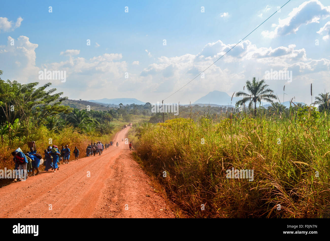 Les travailleurs et les étudiants marchant sur un chemin de terre rouge terre en milieu rural en Afrique Banque D'Images