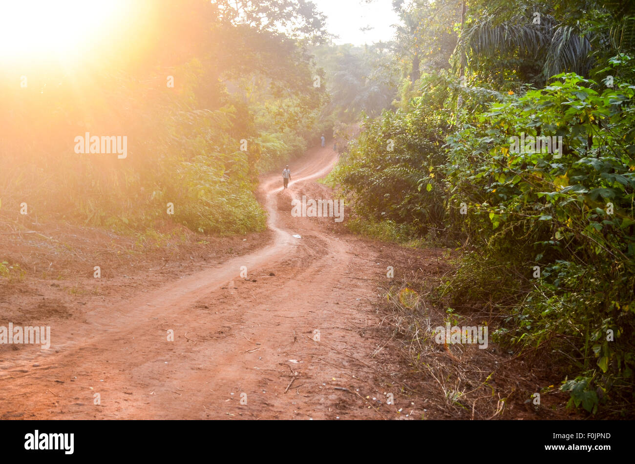 Homme africain local marche sur une terre rouge route de terre en milieu rural en Afrique Banque D'Images