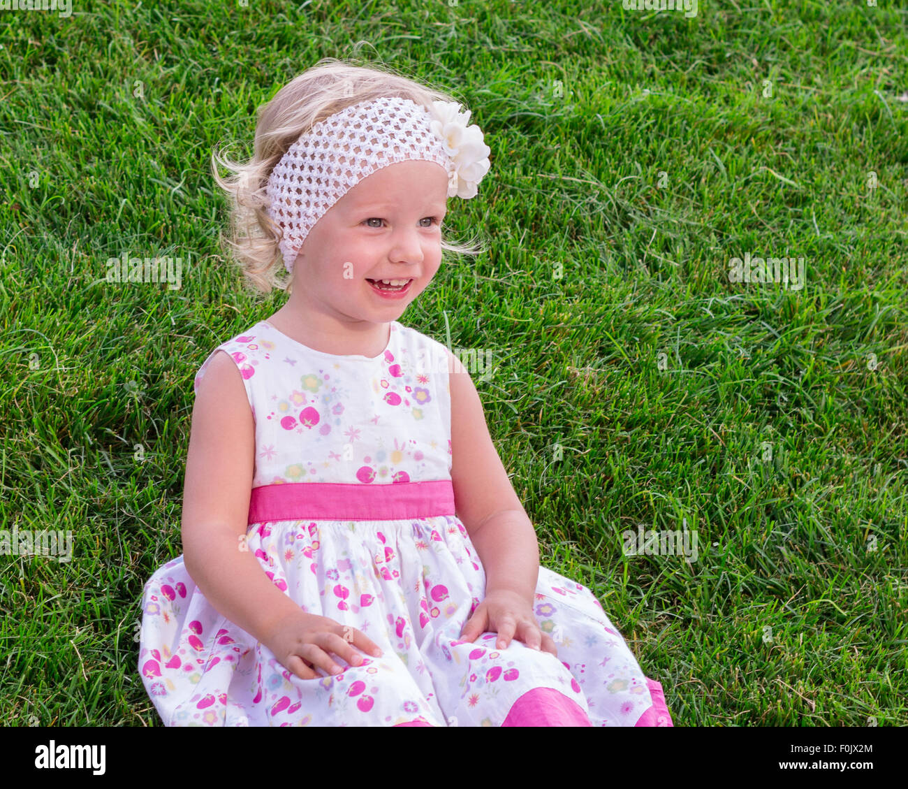 Peu de belle fille assise sur l'herbe verte à l'extérieur dans le jardin d'été. Banque D'Images