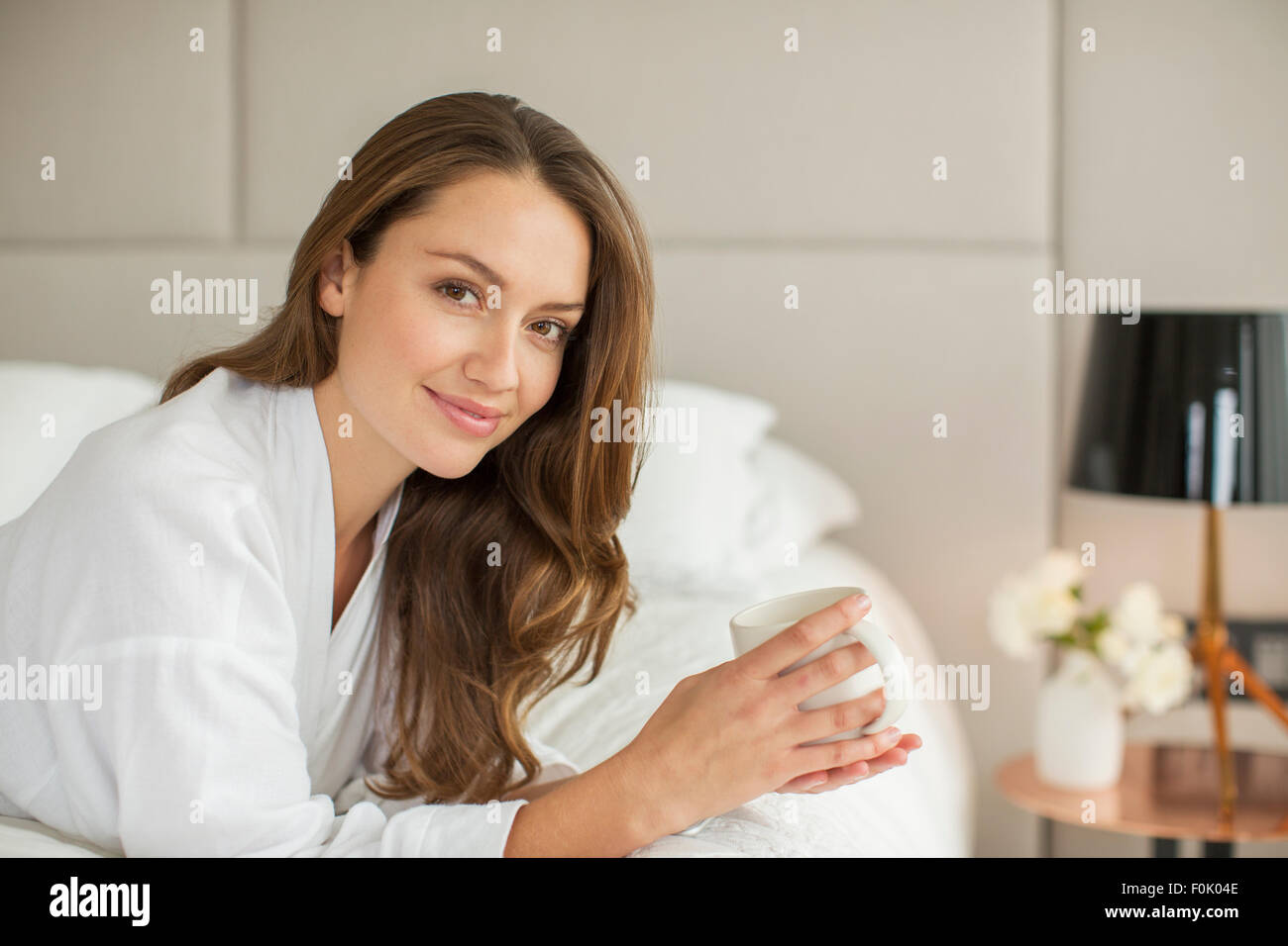 Portrait of smiling woman in bathrobe drinking coffee on bed Banque D'Images