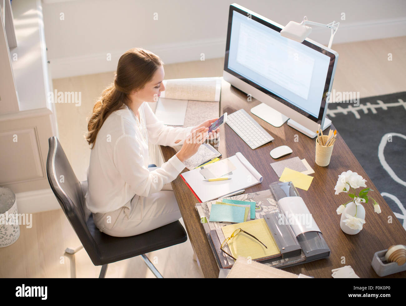 Le designer d'intérieur texting on cell phone at desk in office Banque D'Images