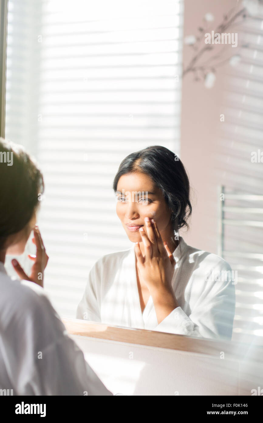 Woman applying moisturizer à face à miroir de salle de bains Banque D'Images