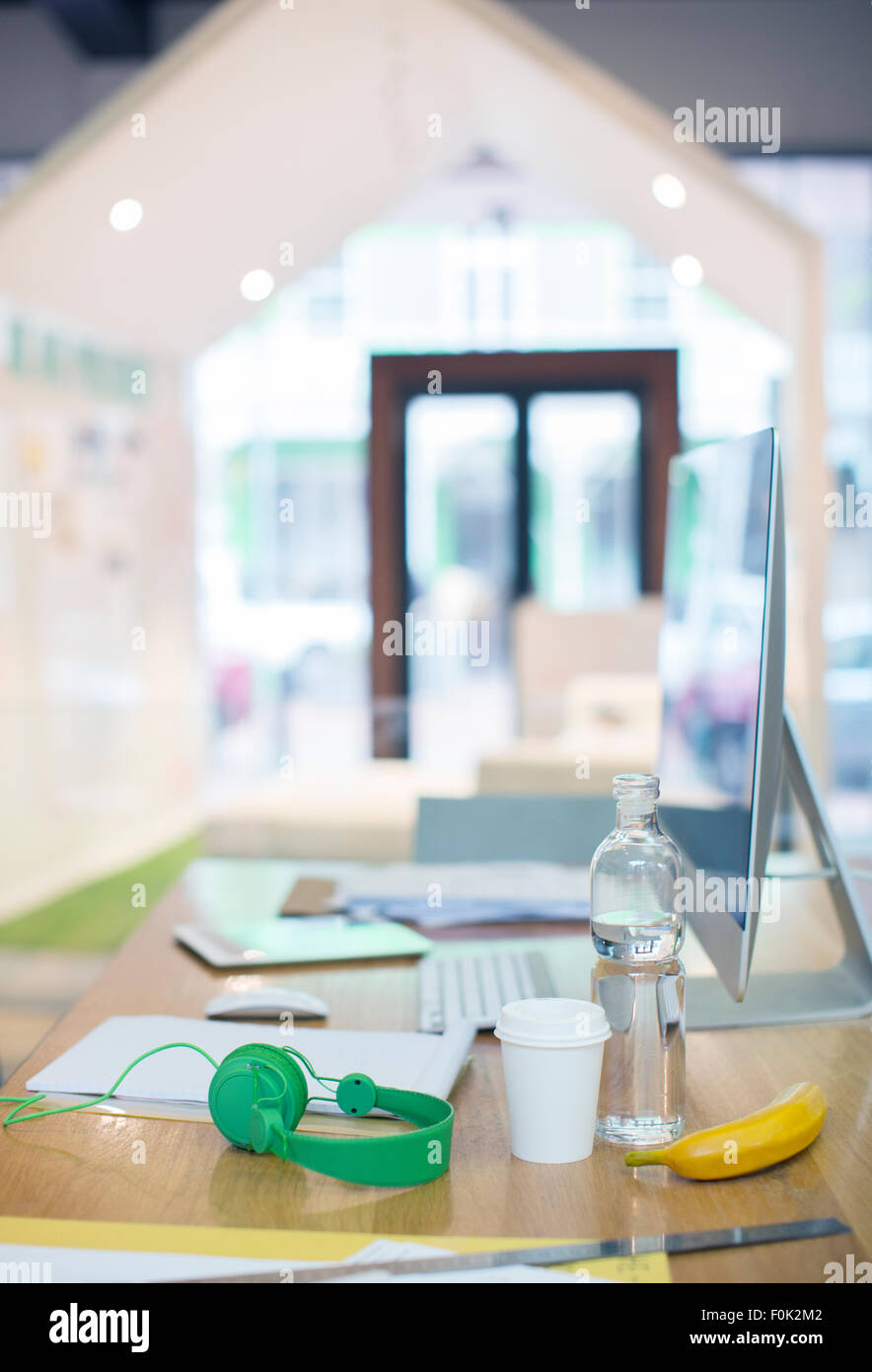 Un casque, une bouteille d'eau, de café et de banane sur bureau avec ordinateur Banque D'Images