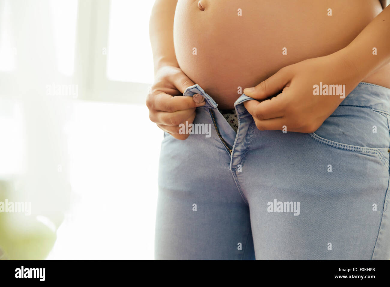 Femme enceinte bouton essaie de son jean, close-up Banque D'Images