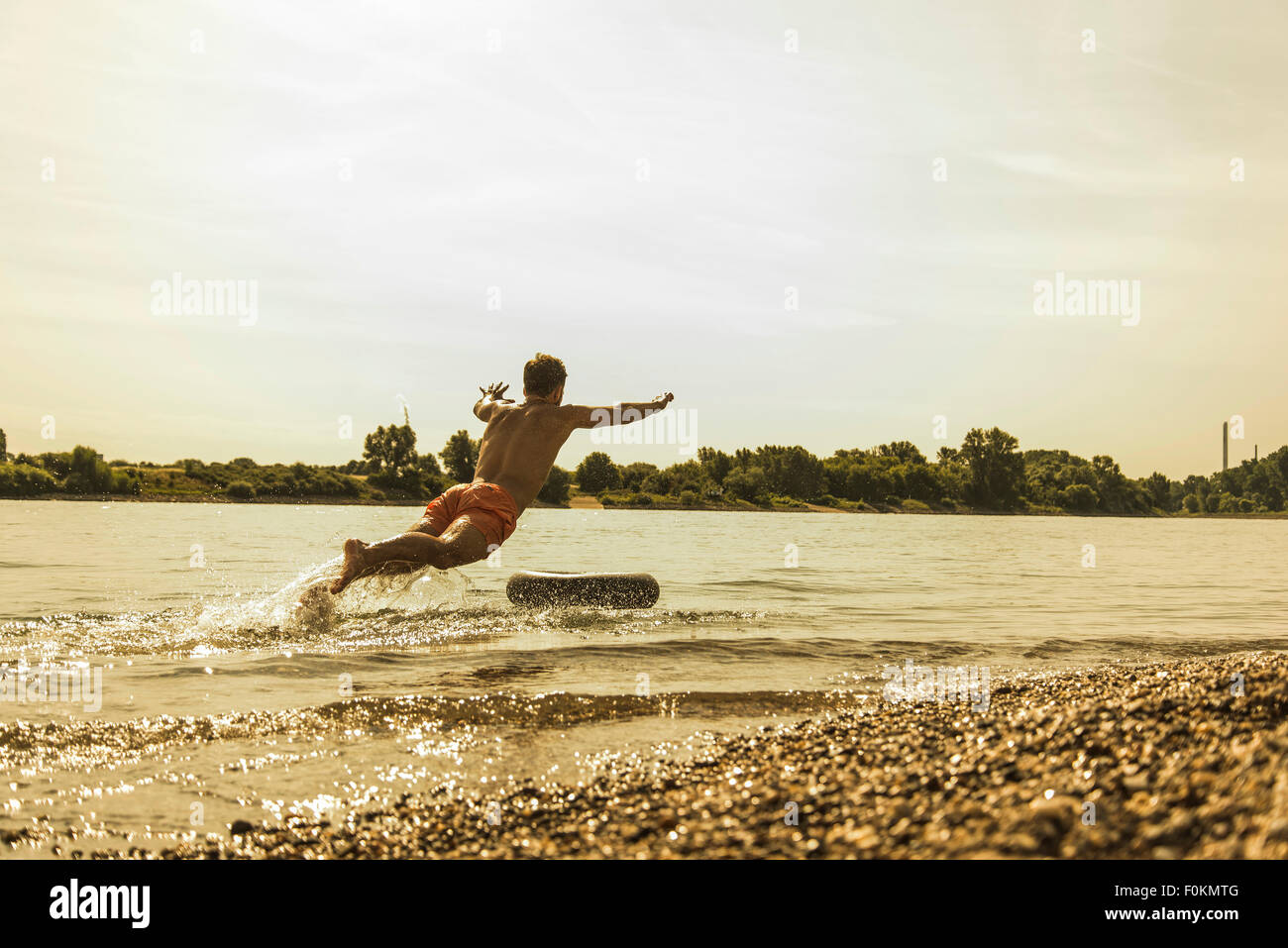 Jeune homme sautant dans la rivière avec tube intérieur Banque D'Images