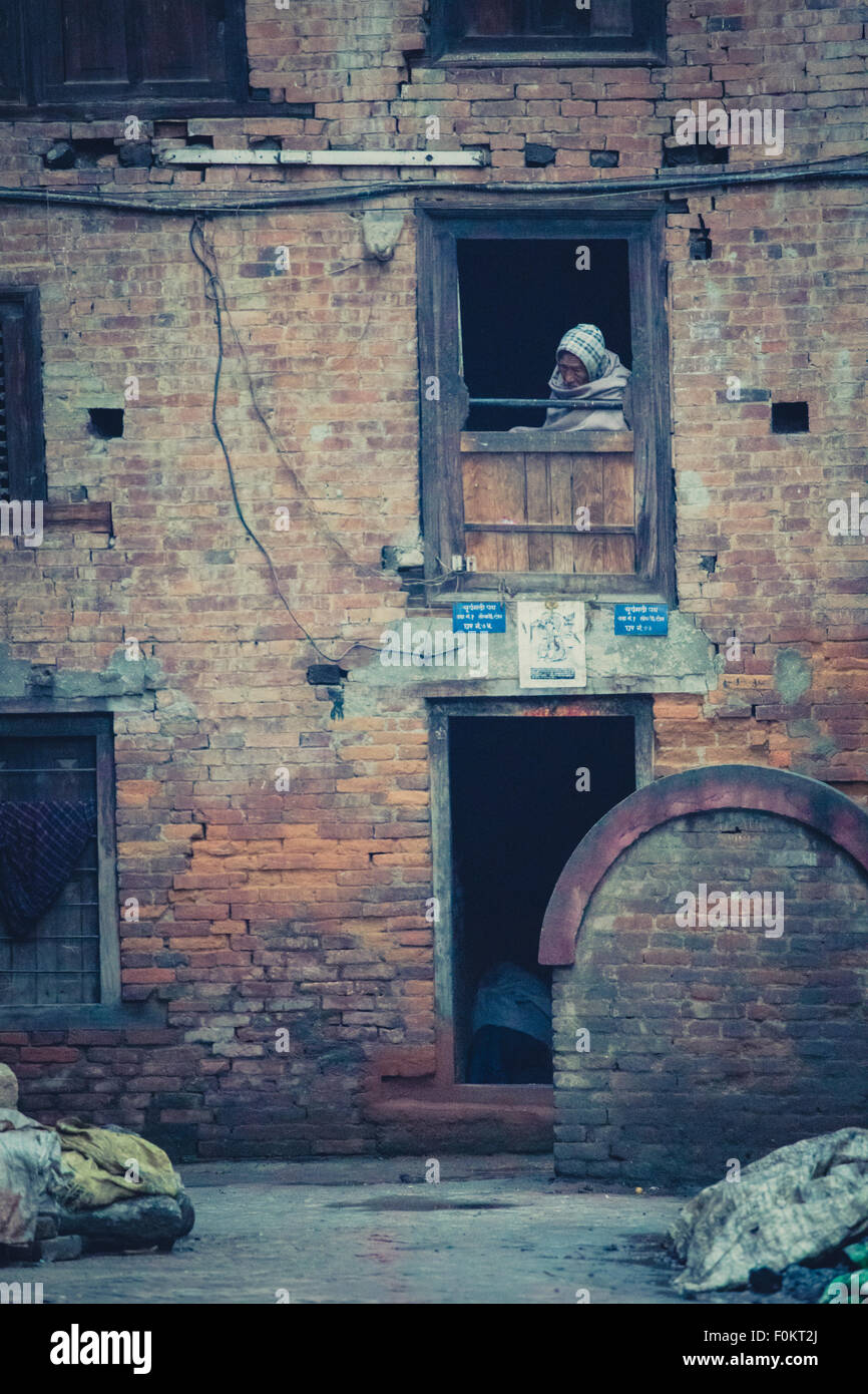 Vieux bâtiment dans le centre historique de Bhaktapur avec vieil homme regardant à travers la fenêtre. Site du patrimoine de l'UNESCO. Banque D'Images