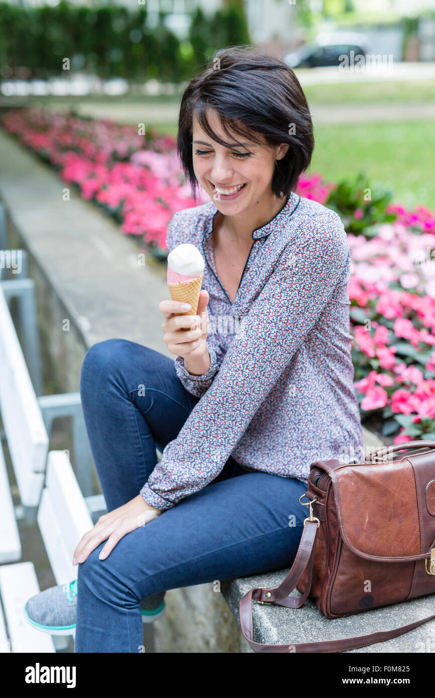 Smiling woman sitting on bench et eating ice cream Banque D'Images