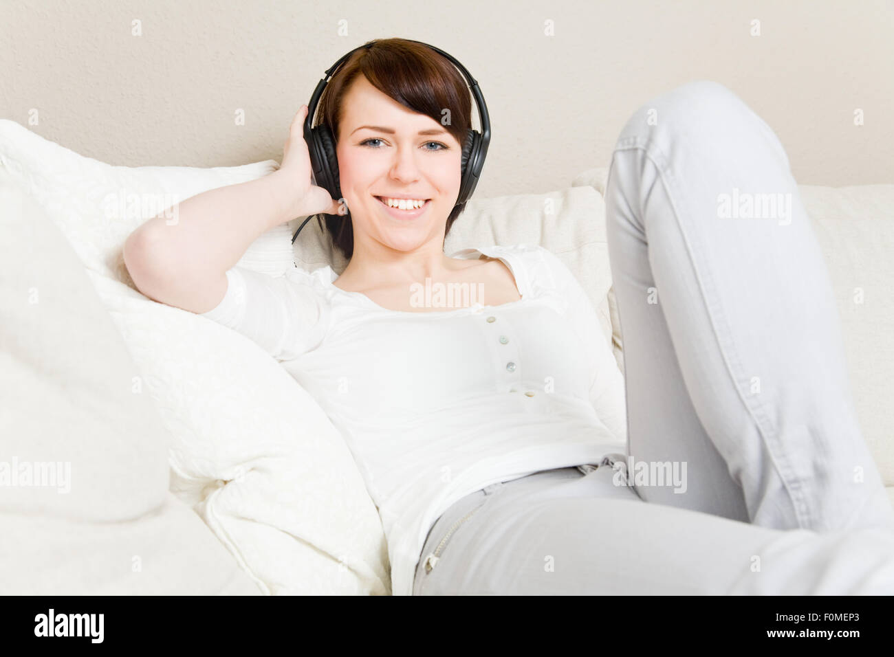 Jeune femme sur un canapé à écouter de la musique avec des écouteurs Banque D'Images