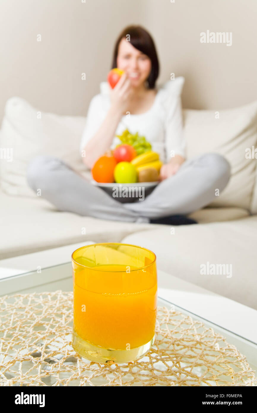 Jeune femme assise en tailleur et manger des fruits avec du jus d'orange sur une table Banque D'Images