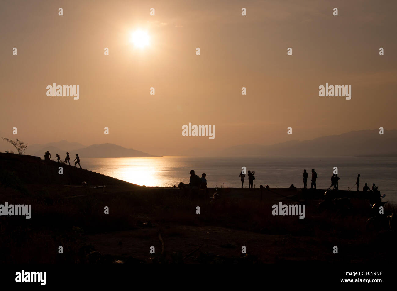 Les gens silhouette sur le ciel clair avant le coucher du soleil à une plage tropicale. Banque D'Images