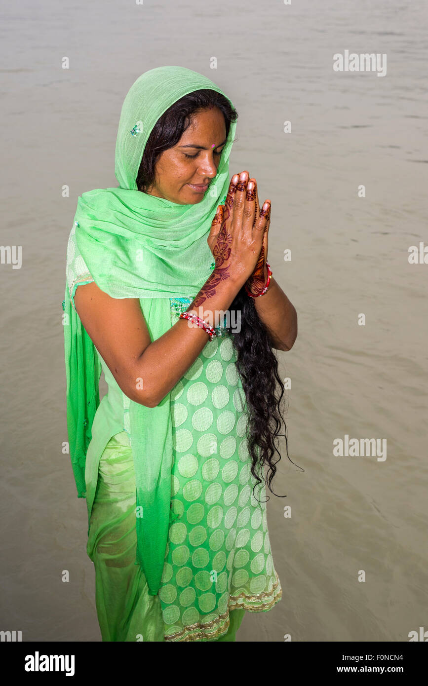 Une jeune femme avec de longs cheveux noirs, mains peintes au henné et une robe verte est priant au ghats du fleuve saint Ganges Banque D'Images