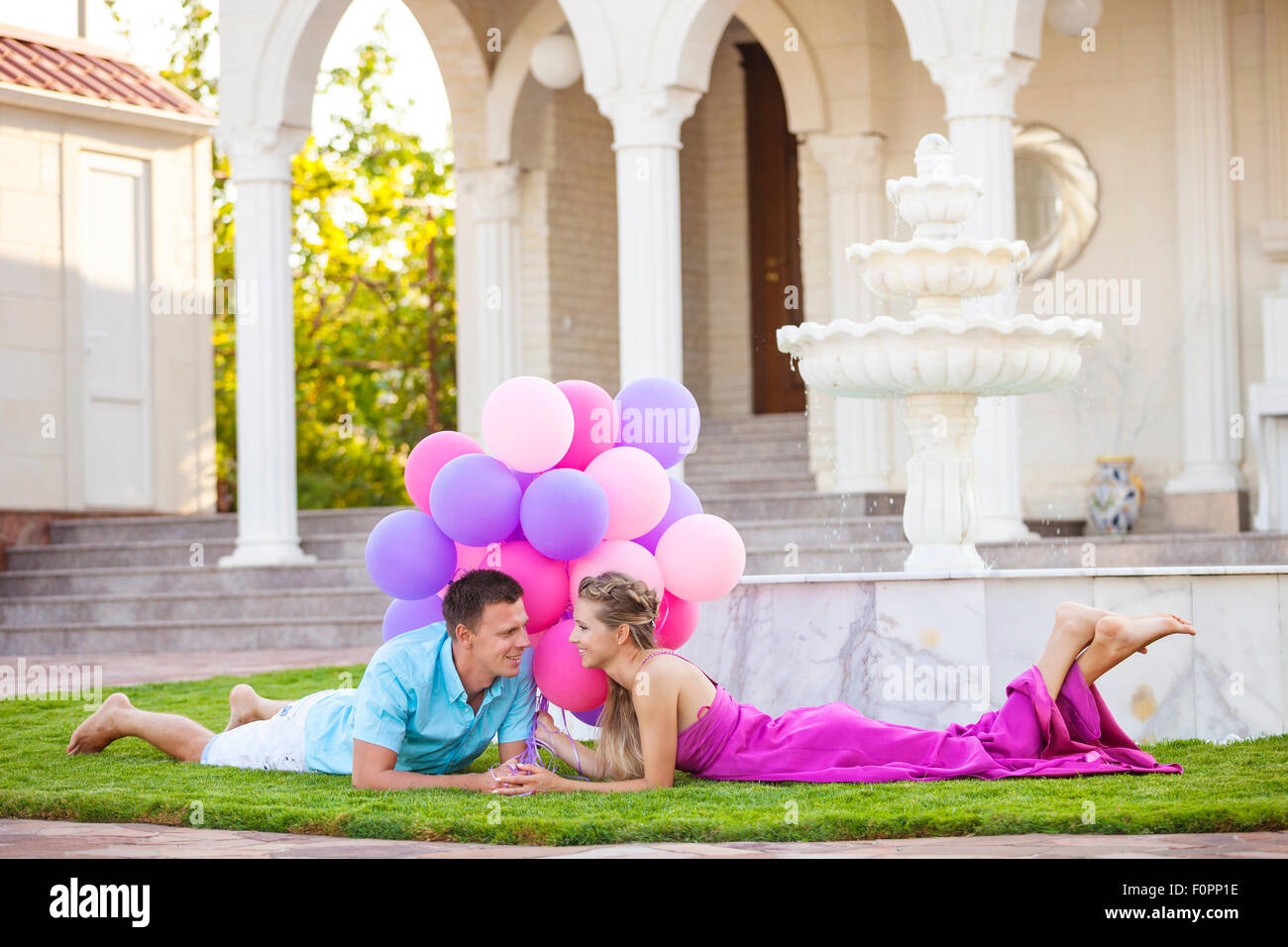 Happy young couple allongé sur la pelouse en face de leur villa et holding colorful balloons Banque D'Images