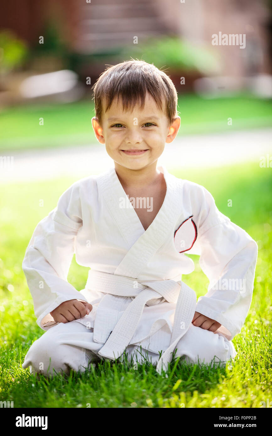 Smiling little boy en kimono sitting on grass in park Banque D'Images