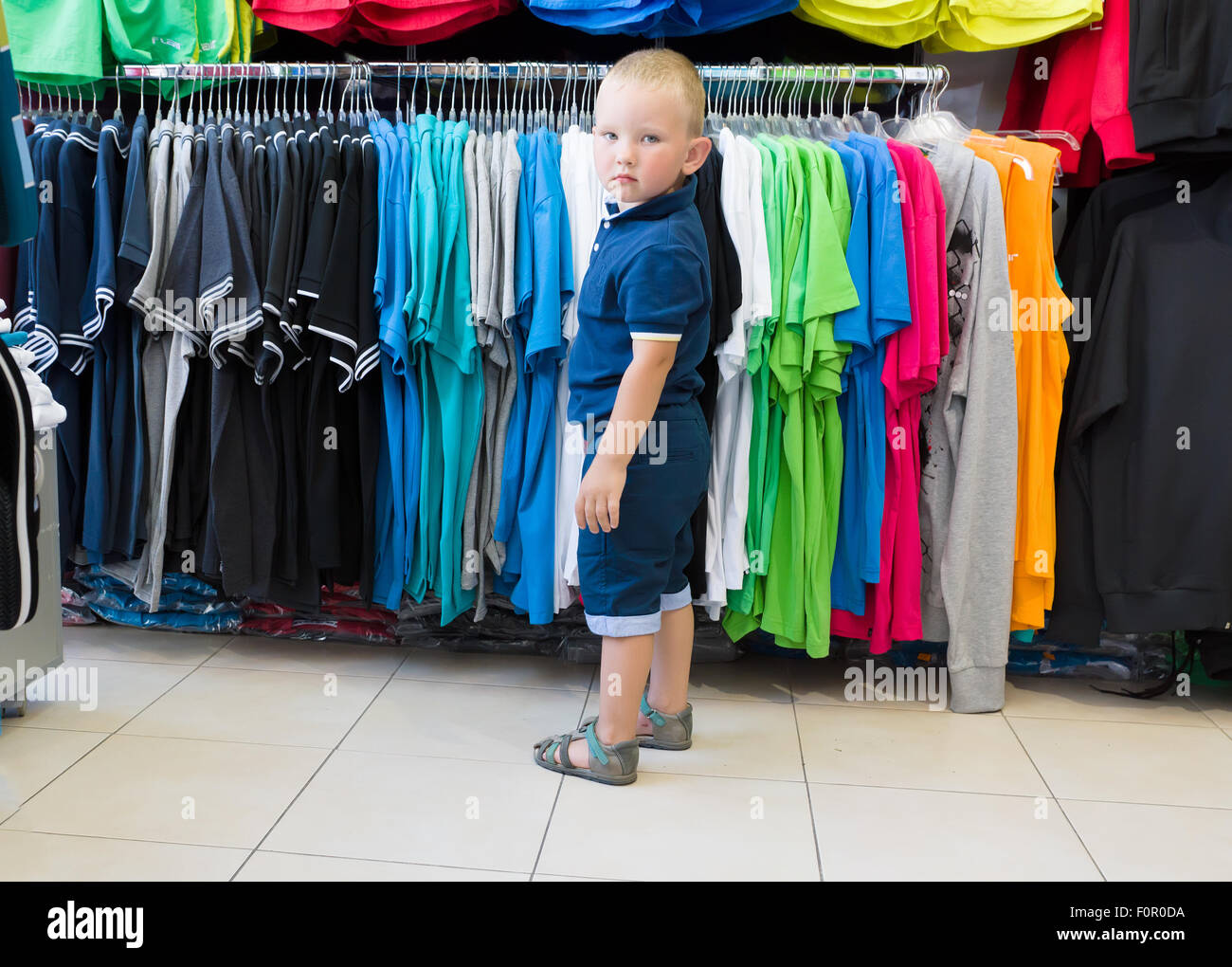 Le petit garçon en short et une chemise choisit une boutique de maillot Banque D'Images