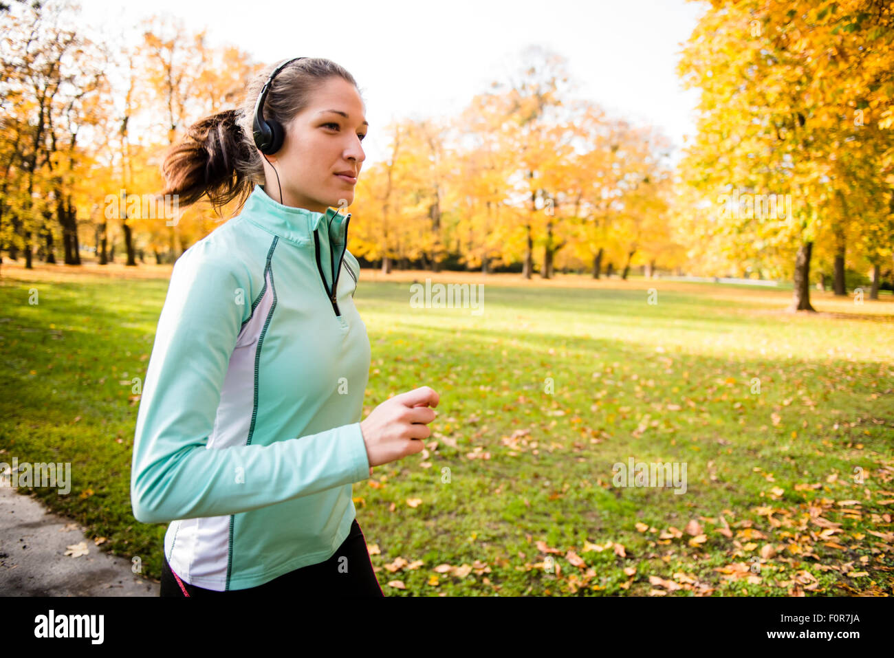 Jeune femme avec des écouteurs le jogging dans la nature de l'automne et à l'écoute de la musique Banque D'Images