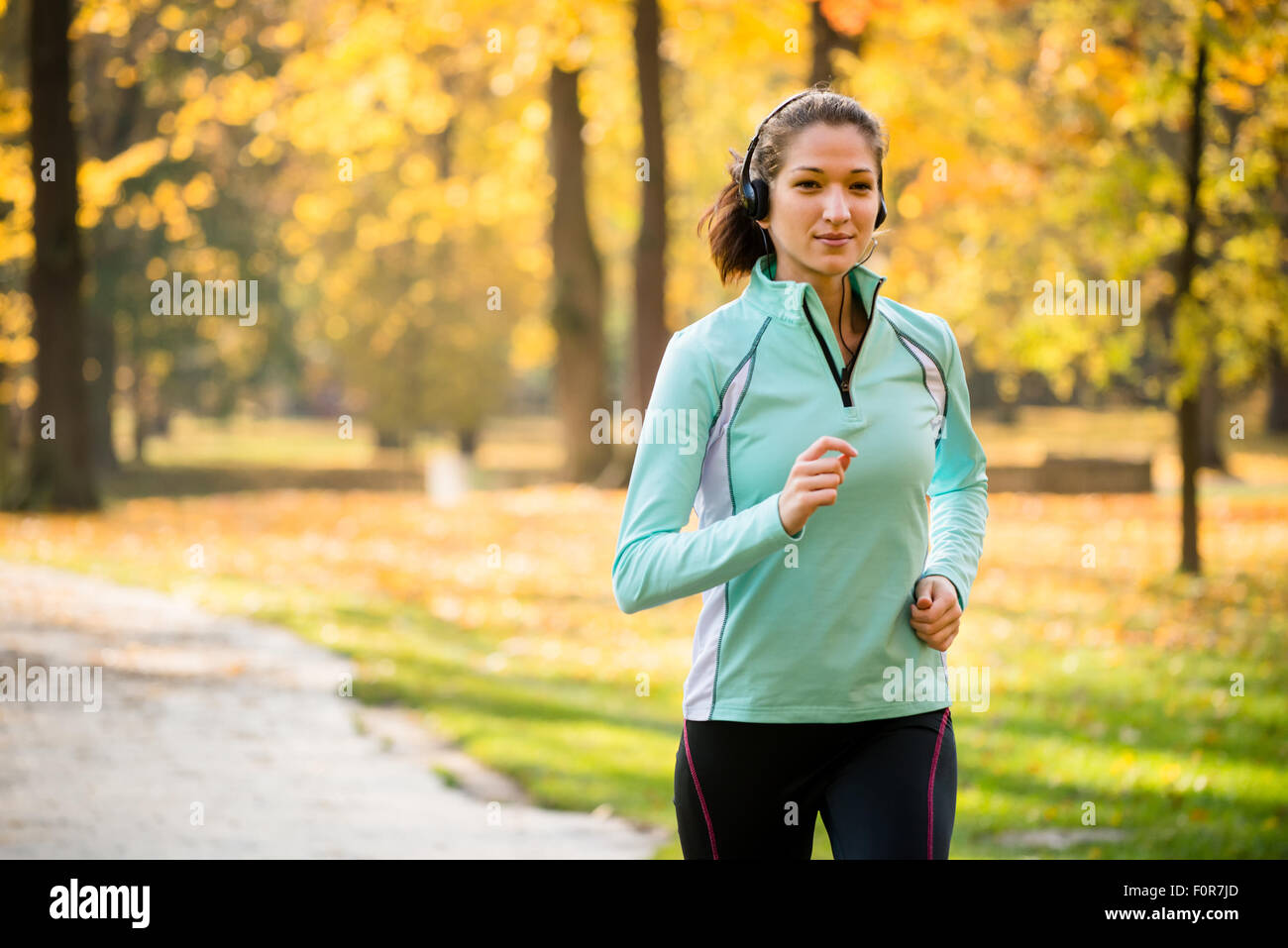 Jeune femme avec des écouteurs le jogging dans la nature de l'automne et à l'écoute de la musique Banque D'Images
