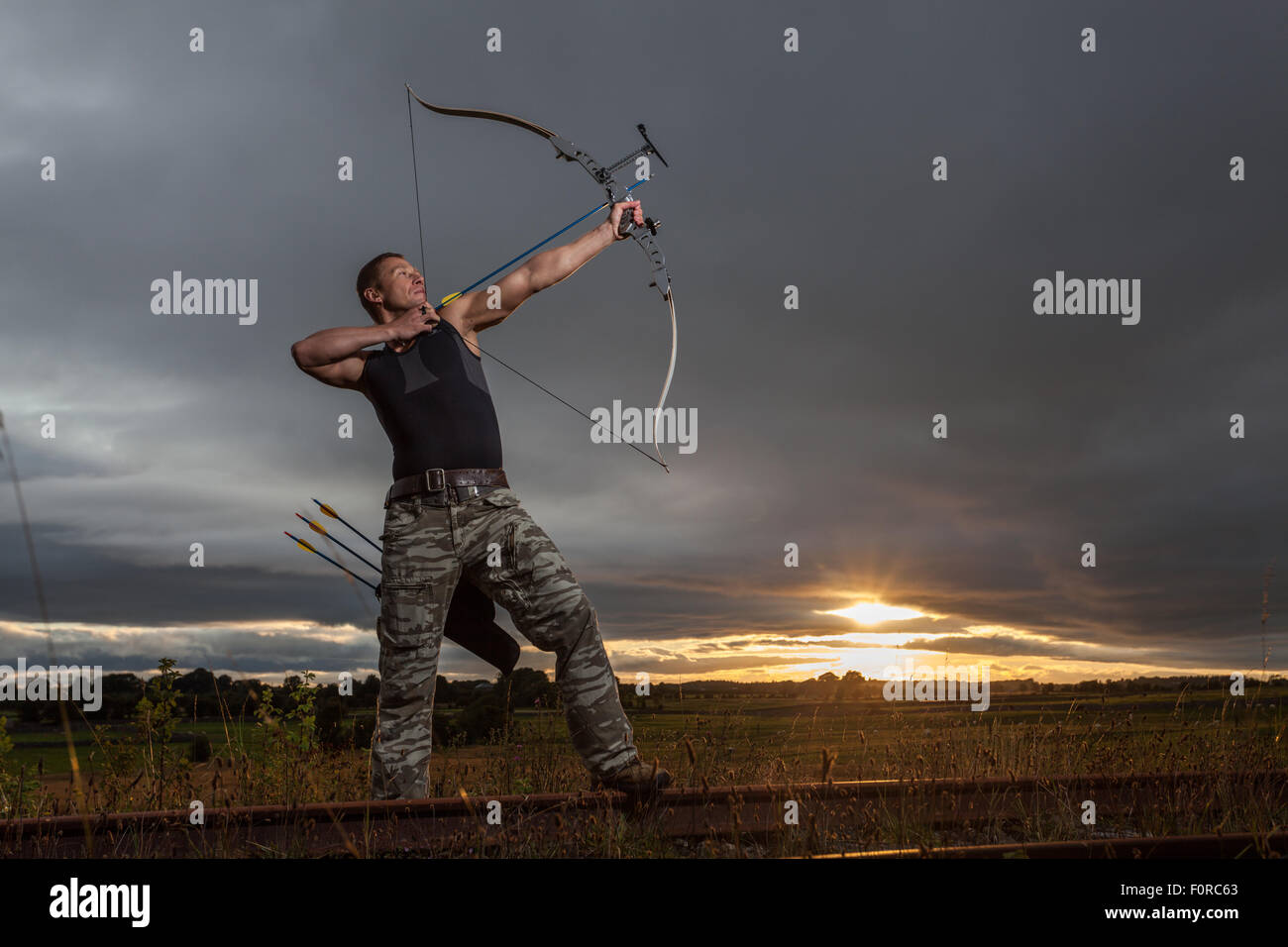 Homme dur avec arc et flèches pendant le coucher du soleil nuageux spectaculaires. Banque D'Images