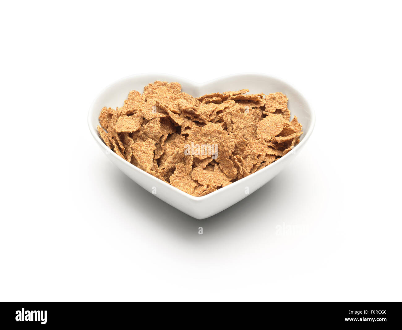 Un simple coup de bol de céréales en forme de coeur plein de céréales de flocons de son sur un arrière-plan uni, blanc et un chemin de détourage. Banque D'Images