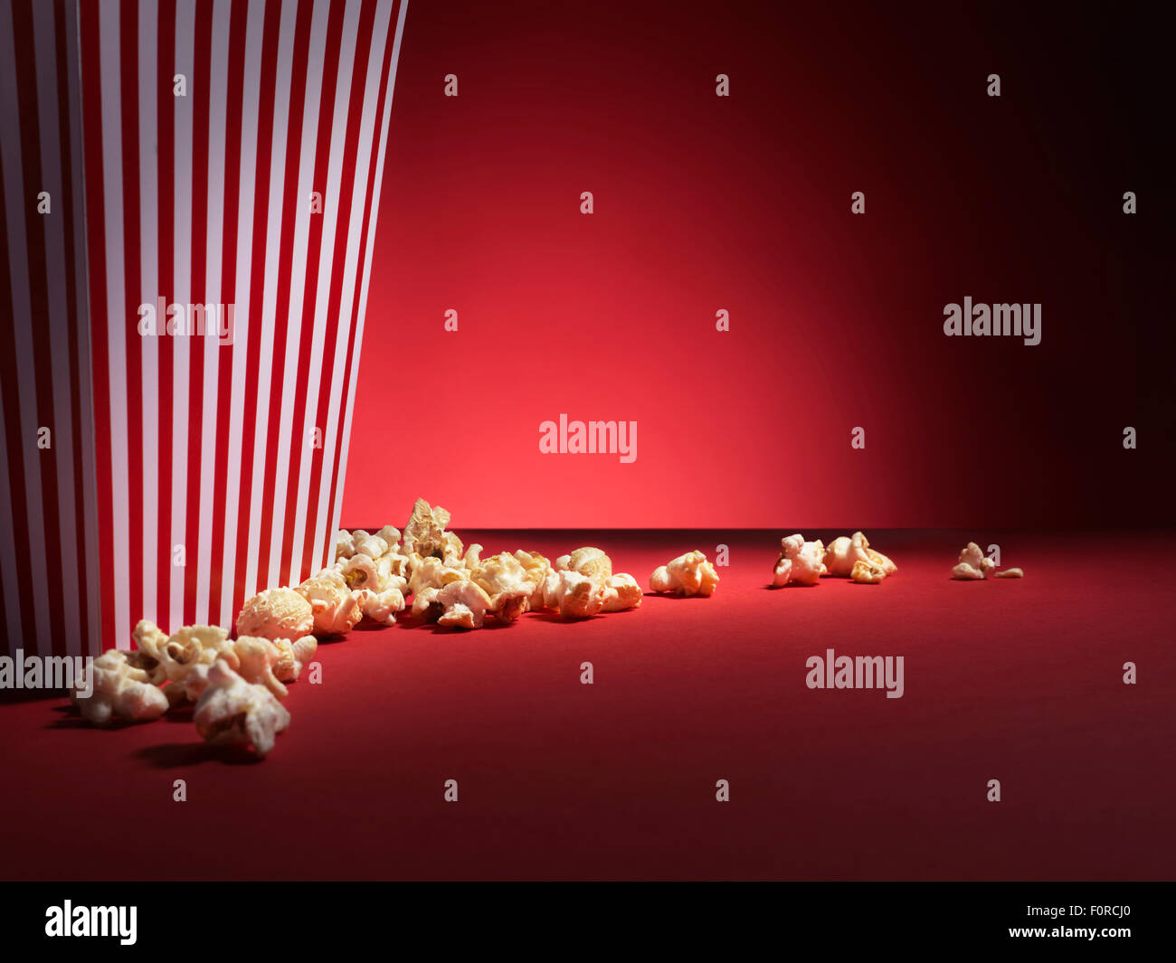 Rapprochée sur une boîte de popcorn popcorn avec éparpillés autour de sa base. Tourné sur un fond rouge, spotlit, vignette fond style avec pl Banque D'Images