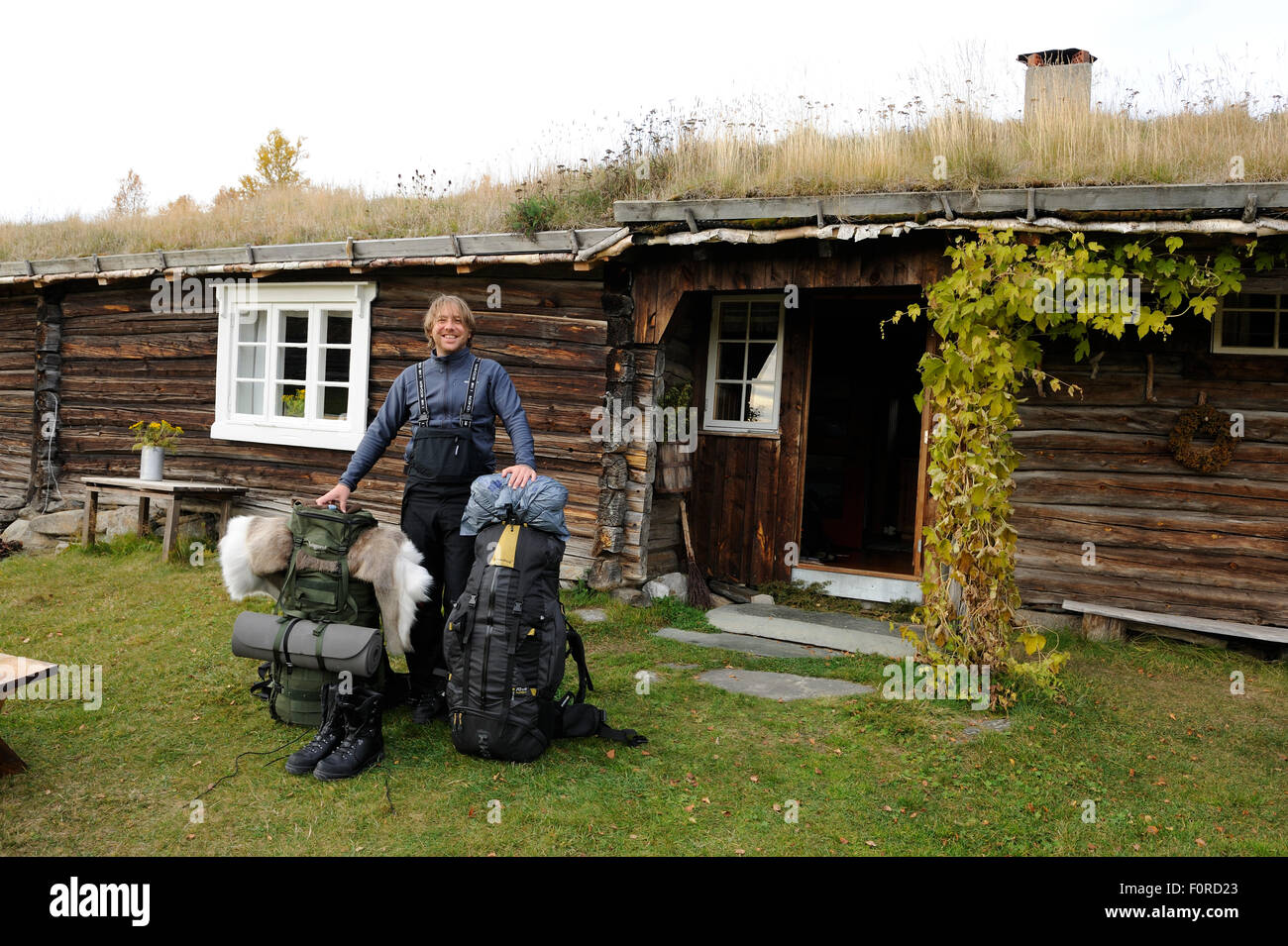 Laurent Joffrion avec deux sacs à dos, debout à l'extérieur de bâtiment traditionnel avec toit d'herbe, le Parc National de Forollhogna, Norvège, septembre 2008 Banque D'Images