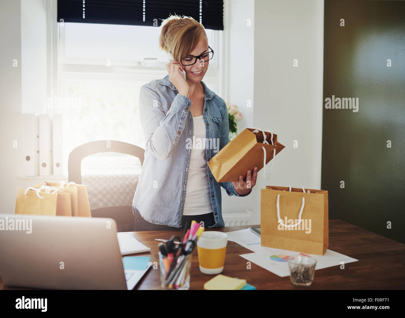 La passation d'ordres motivés businesswoman au téléphone pour l'emballage pour son nouveau magasin en ligne basé sur le web comme elle est titulaire d'un brown pa Banque D'Images