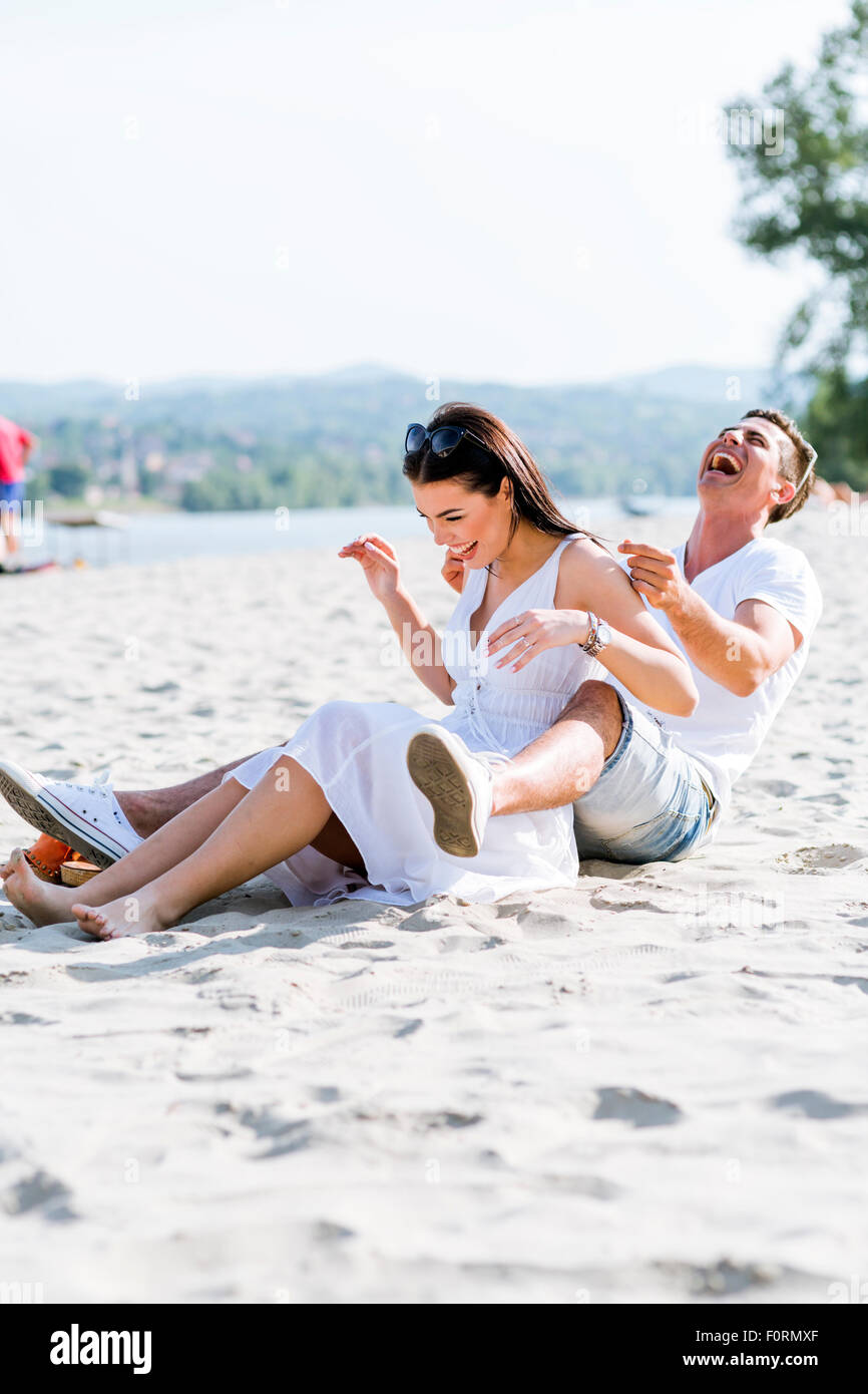 Couple amoureux assis à une plage de sable fin et souriant Banque D'Images