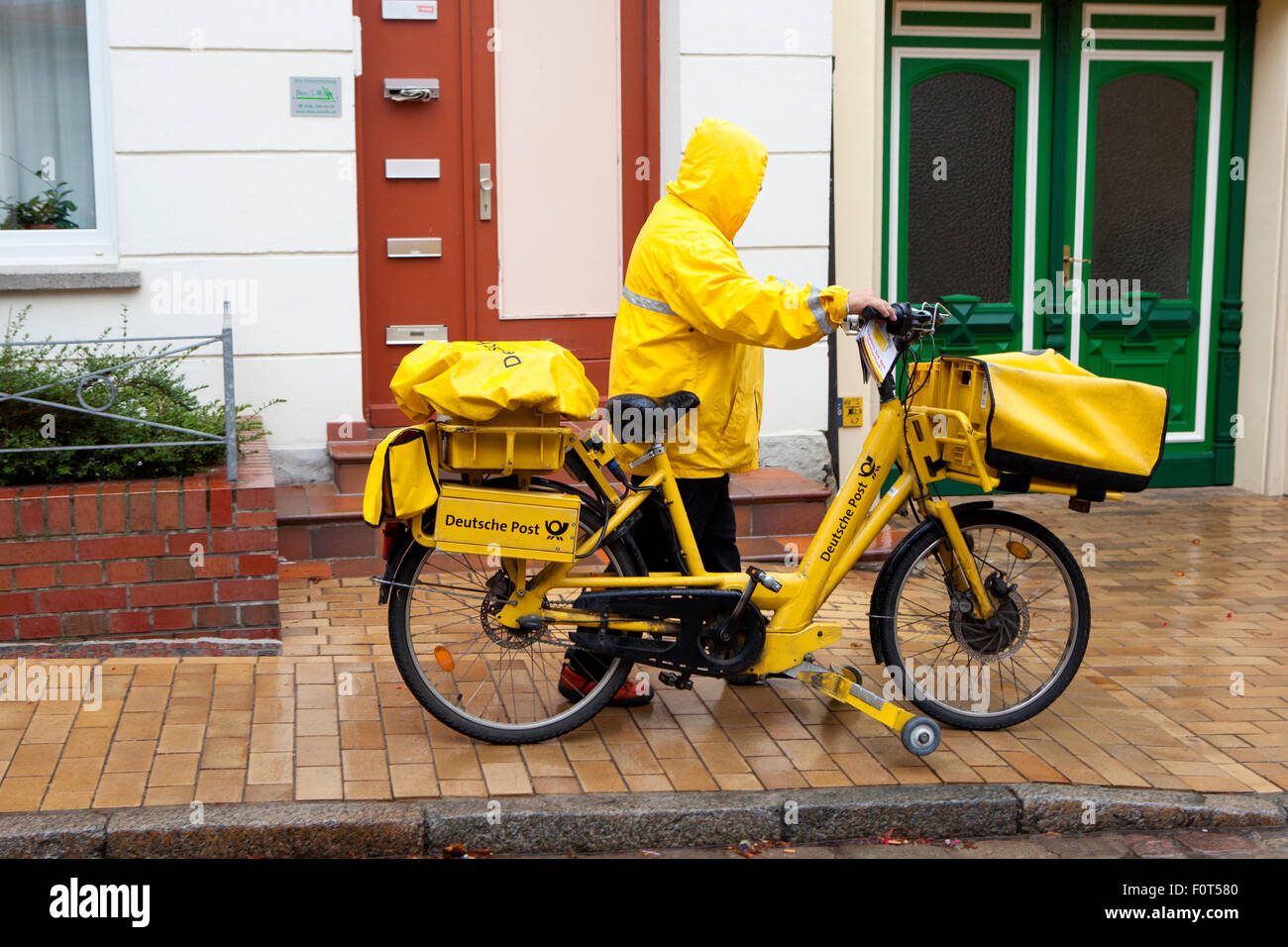 Livraison jaune vélo et postman par Deutsche Post DHL plus grand fournisseur d'offrir sous la pluie Banque D'Images