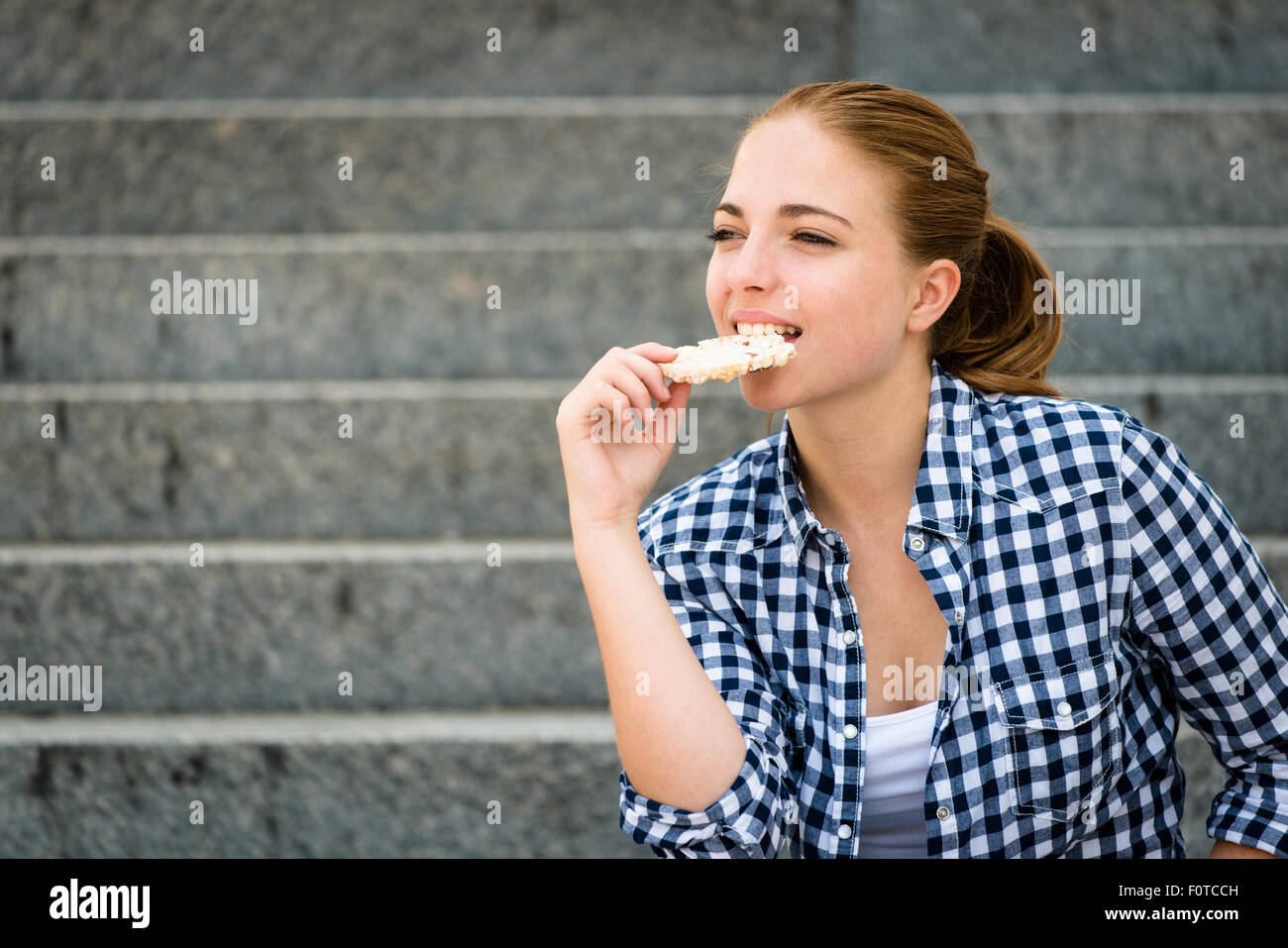 Mode de vie sain - manger du pain soufflé adolescent assis sur des escaliers extérieurs Banque D'Images